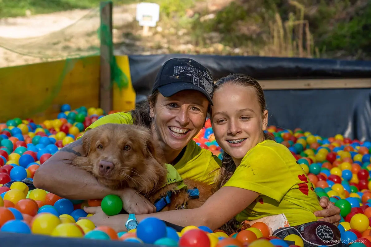 Frau, Mädchen und Hund liegen lachend im Bällebad